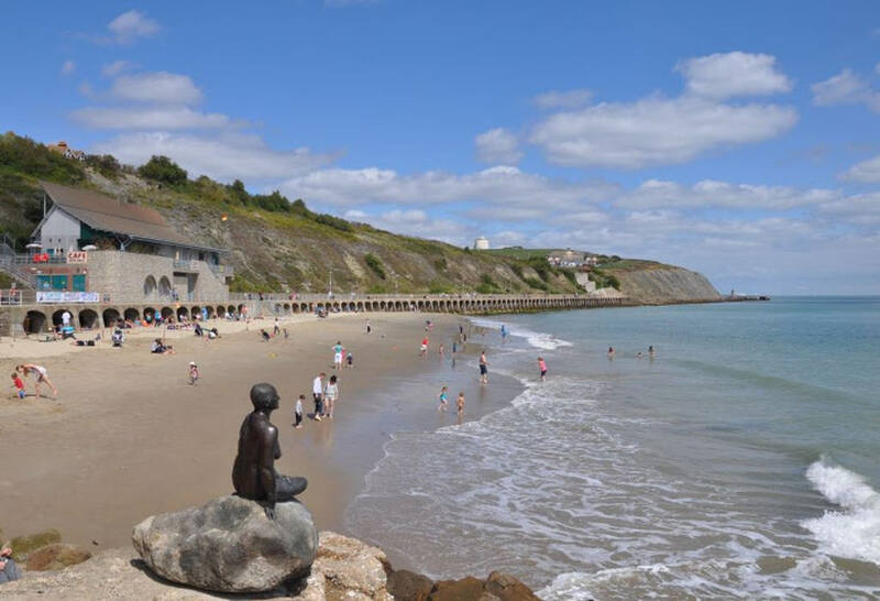 Ein Sandstrand mit grünbewachsenen Felsen direkt am Meer