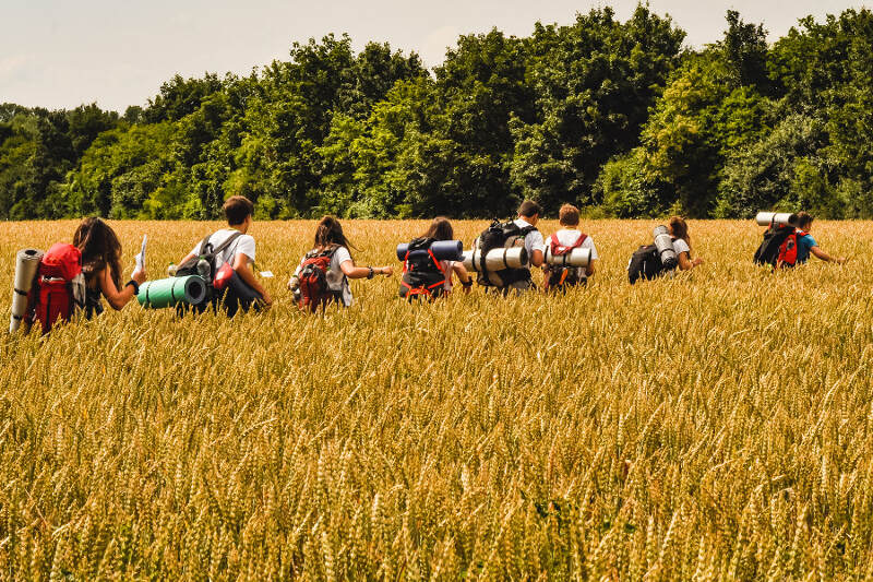 Jugendliche ziehen mit vollgepackten Rucksäcken durch Felder im Abenteuercamp
