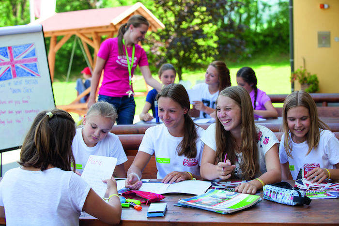 Teilnehmer eines Ferienprogramms Stadt Salzburg sitzen lachend an einem Tisch und haben Spaß beim Lernen