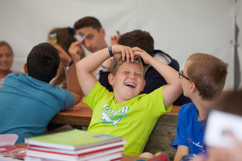 Junge sitzt lachen am Tisch während seines Englisch-Camp Neusiedlersee