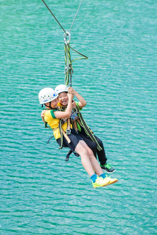 Zwei Kinder hängen gesichert an einer Seilbahn über einem See