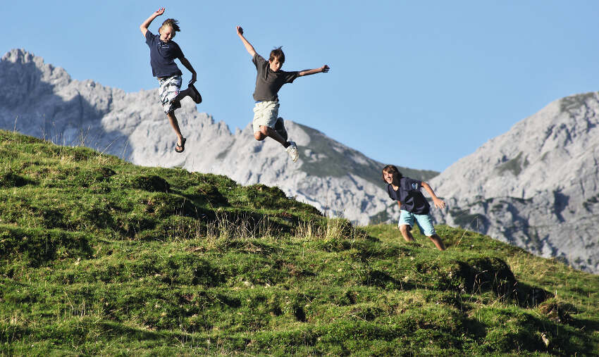Drei Jungen springen im Ferienprogramm Salzburg in die Luft mit den Bergen im Hintergrund