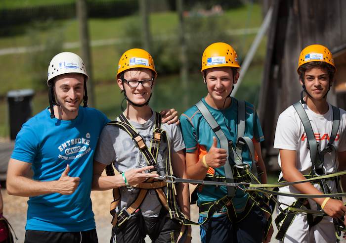 Vier Teilnehmer eines Multi-Activity-Camps tragen Kletterausrüstung und schauen in die Kamera