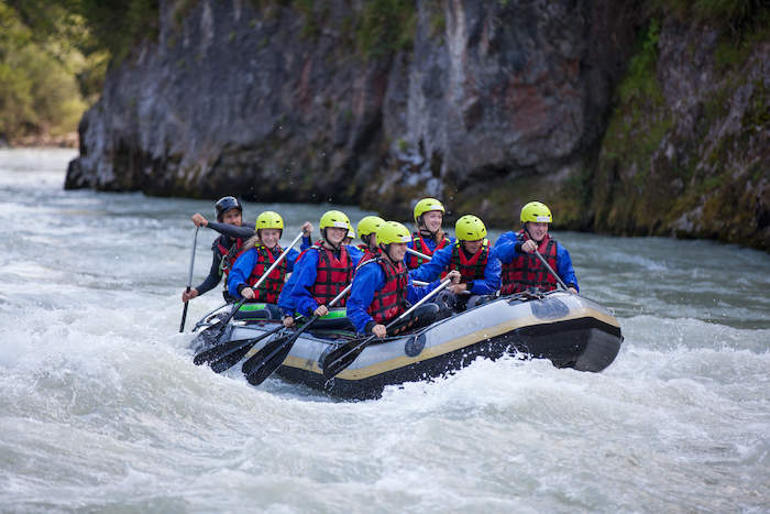 Teilnehmer beim Wasserrafting mit einem gelben Schlauchboot auf einem Fluss im Ferienprogramm Salzburg