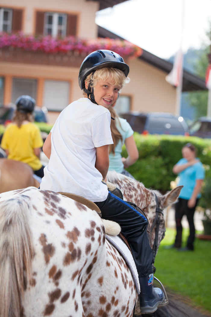 Junge sitzt auf Pferd im Sommercamp Kinder