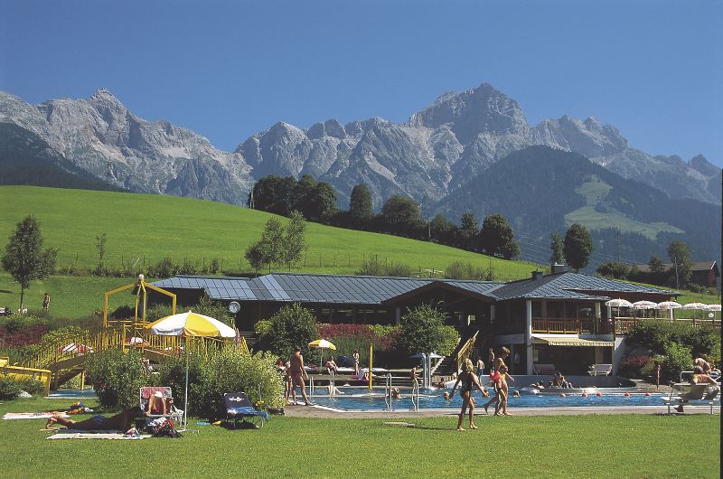 Kinder planschen in einem Schwimmbecken inmitten einer Berglandschaft im Ferienlager Kinder