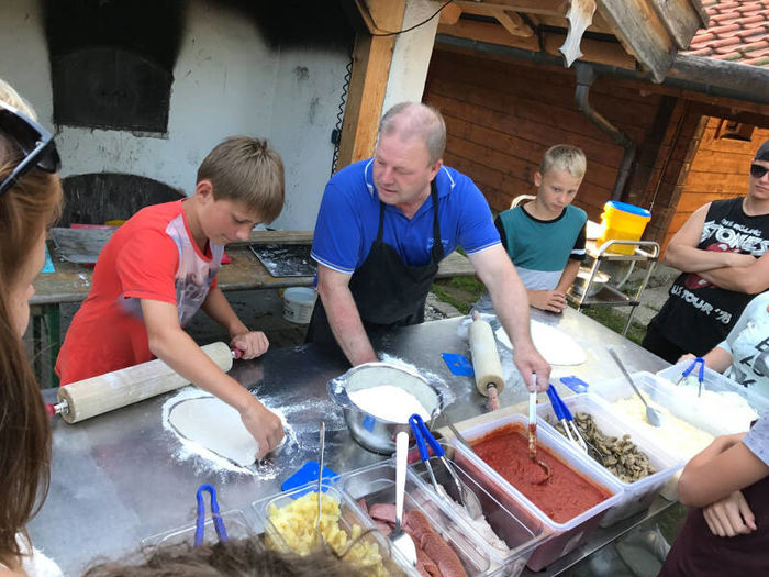 Betreuer und Kinder backen zusammen Pizza im Englisch Feriencamp