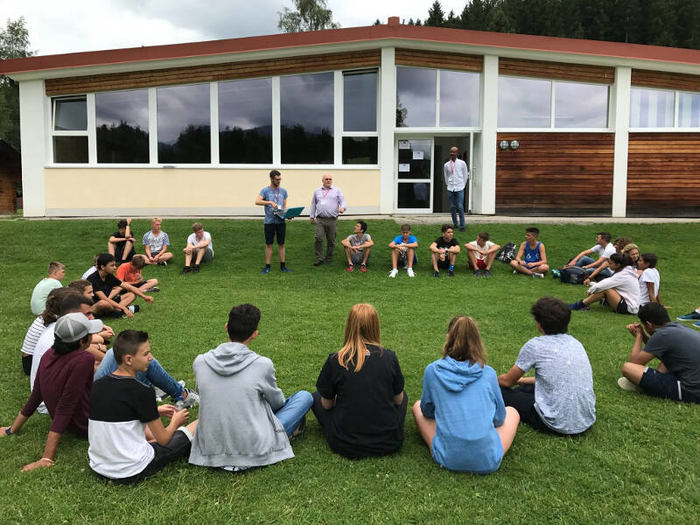 Teilnehmer sitzen im Kreis und Betreuer erklären etwas im Englisch Feriencamp