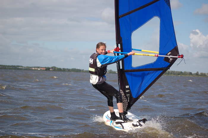 Ein Mädchen der Jugendreisen Norwegen surft auf einem Windsurfbrett