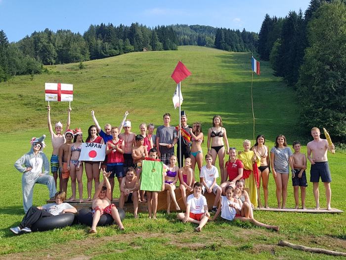 Die Teilnehmer des Englisch-Camps Oberösterreich posieren auf einem Gruppenfoto mit mehreren Fahnen und Verkleidungen