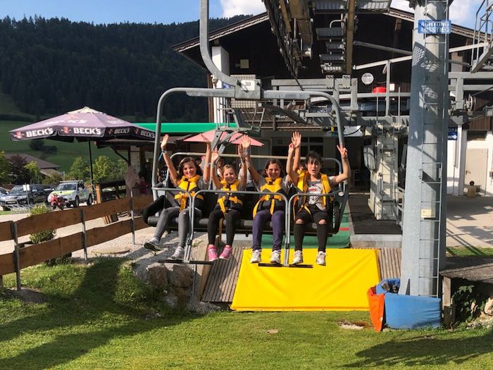 Mädchen fahren in einem Sessellift im Englisch-Camp Tirol
