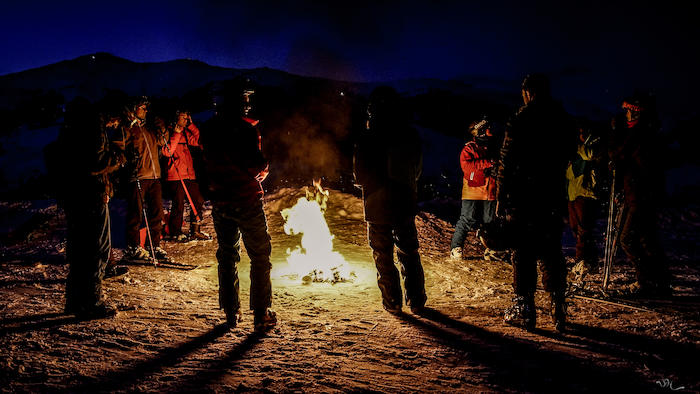 Teilnehmer bei einem Ski-Camp wärmen sich am Lagerfeuer