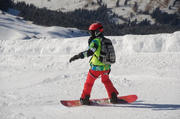 Im Skiurlaub Semesterferien fährt ein Junge mit seinem Snowboard den Berg hinunter