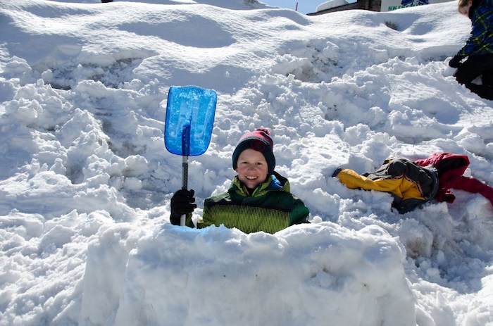 Im Juvigo Skilager sitzt ein Junge mit seiner Schaufel in einem Schneehaufen