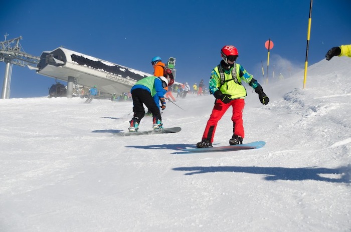 Die Teilnehmer des Skiurlaubs Semesterferien fahren mit Snowboard auf der Piste bei blauem Himmel und Sonnenschein