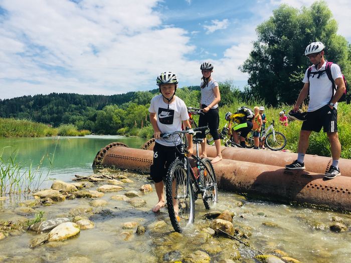 Jugendliche bei einer Radtour durchs Wasser im Sommercamp am Wolfgangsee