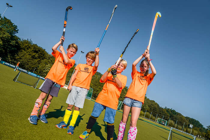 Kinder halten Hockeyschläger in die Luft im Sport Feriencamp