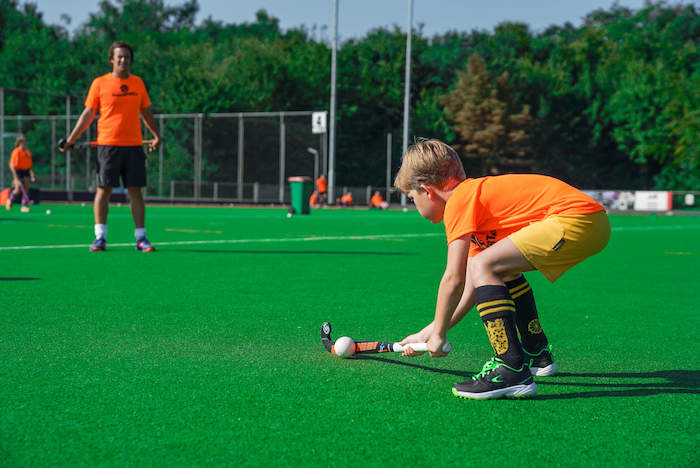 Junge schlägt Hockeyball im Sport Feriencamp