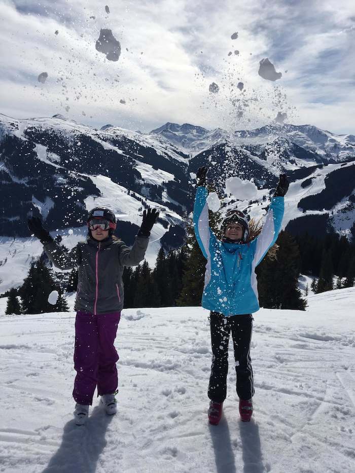 Zwei Teilnehmerinnen der Ferienbetreuung Ostern stehen an einer Skipiste und werfen Schnee in die Luft