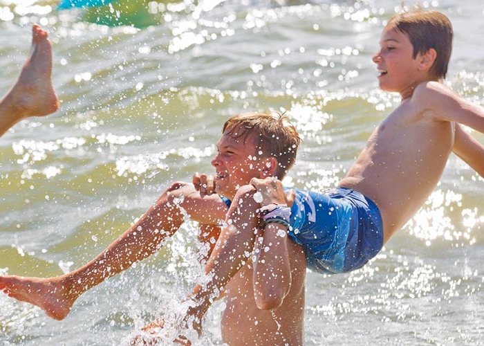 Jungs werfen einander ins Wasser im Jugendcamp