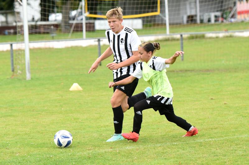 Ein Junge und ein Mädchen spielen während ihres Feriencamps Bayern Fußball und kämpfen um den Ball