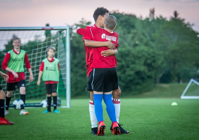 Zwei Jungs der Juvigo Fussball-Camps umarmen sich auf dem Spielfeld