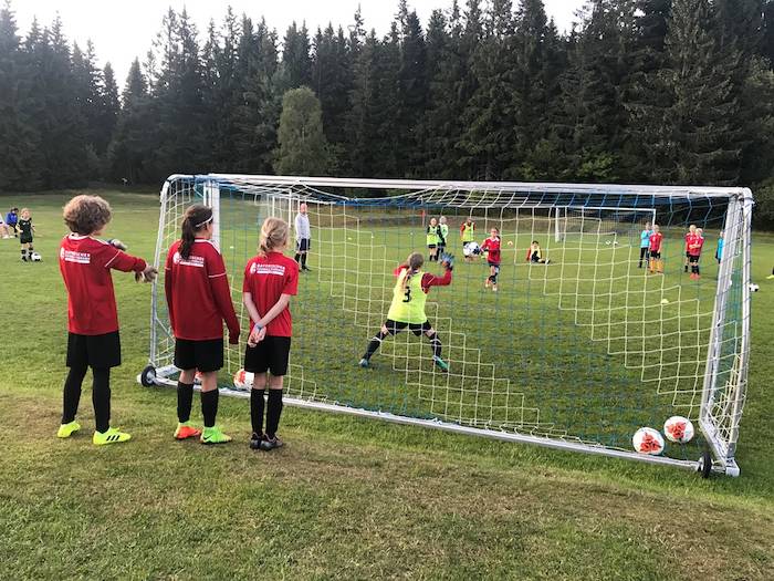 Drei Mädchen stehen hinter dem Tor und schauen ihren Freundinnen beim Fußball spielen zu