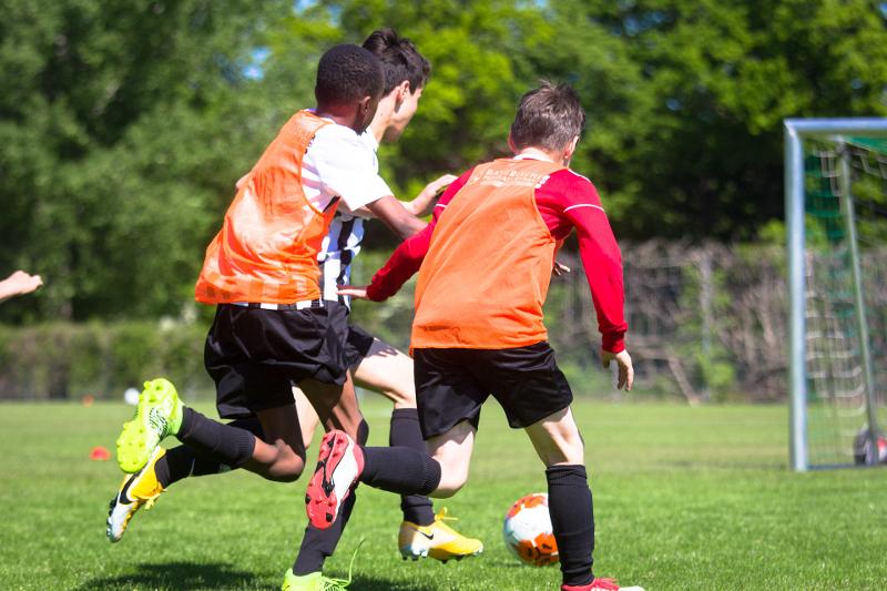 3 Jungen spielen gemeinsam auf einer Wiese Fußball im Feriencamp Last Minute und rennen dem Ball hinterher