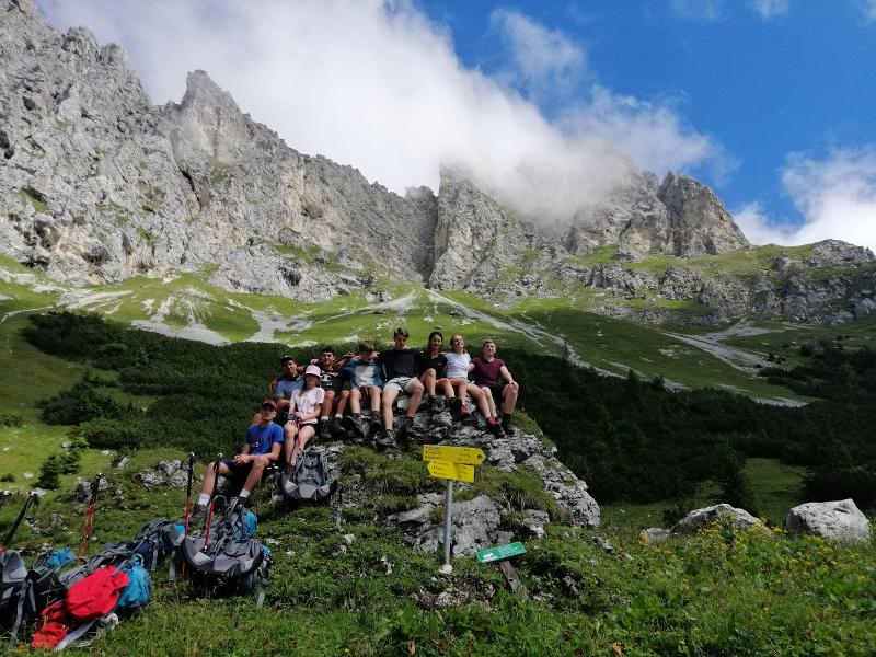Eine Gruppe Jugendlicher sitzt auf einem Felsen vor einem Berg auf einer Wanderung beim Ferienangebot
