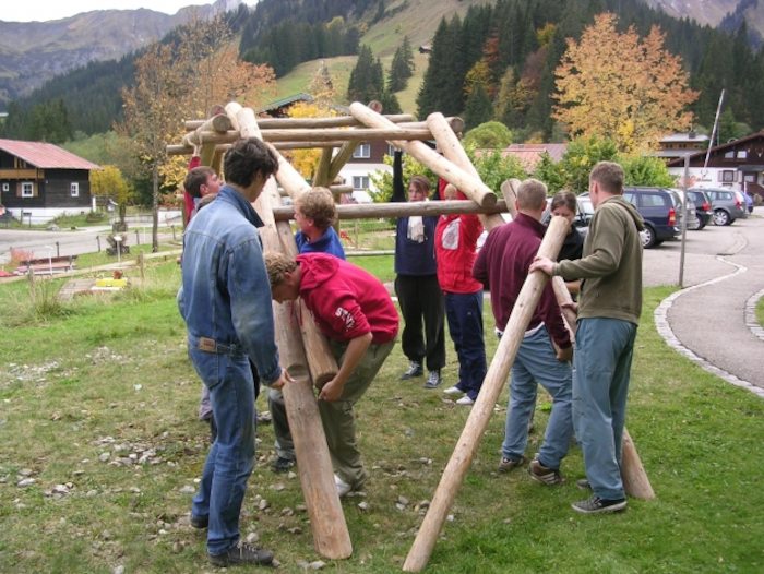 Teilnehmer heben Holzstämme zusammen hoch im Sommercamp Vorarlberg