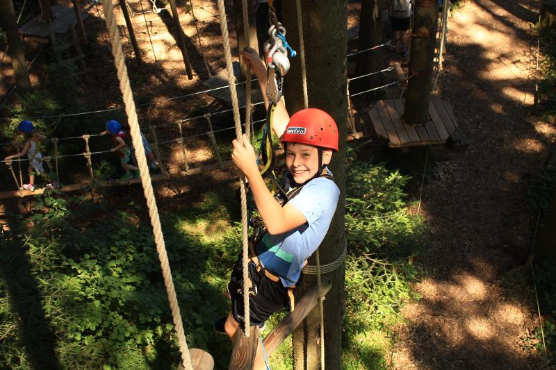 Teilnehmer einer Ferienbetreuung Ostern trägt einen Helm und klettert durch einen Hochseilgarten