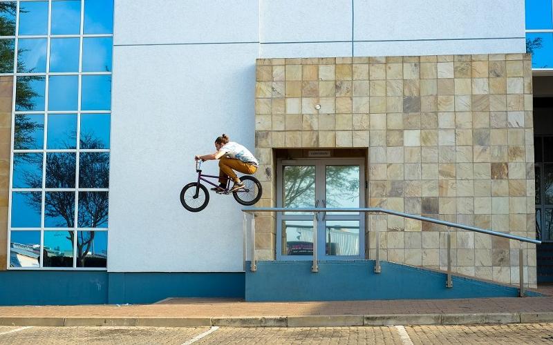 Teilnehmer eines BMX-Camps übt vor einer Hauswand einen Rail-Sprung
