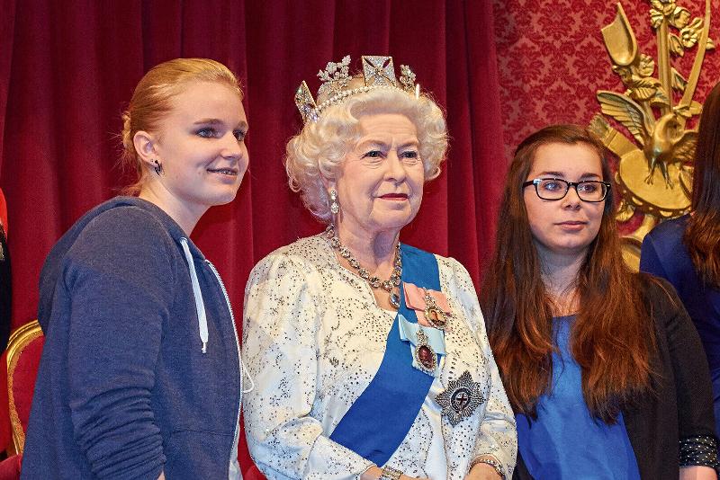 Zwei Mädchen machen ein Selfie mit der Wachsfigur der Queen