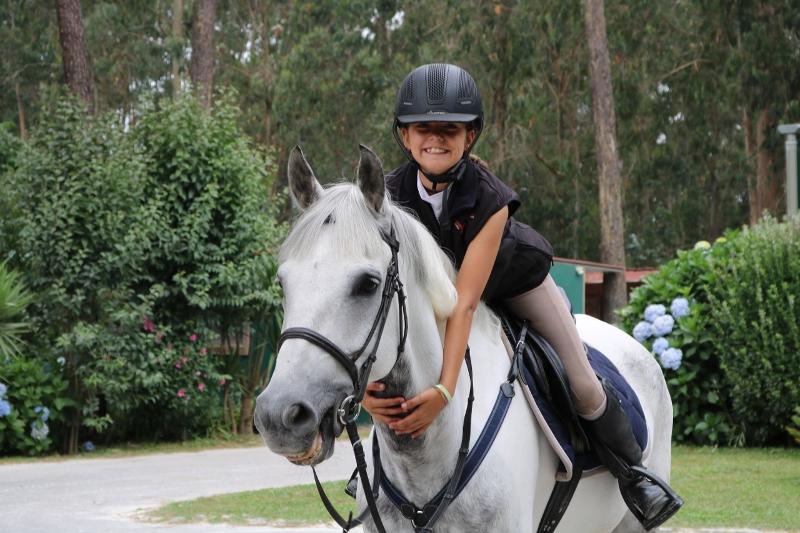 Ein Mädchen des Camps in Portugal sitzt auf einem weißen Pferd und umarmt es