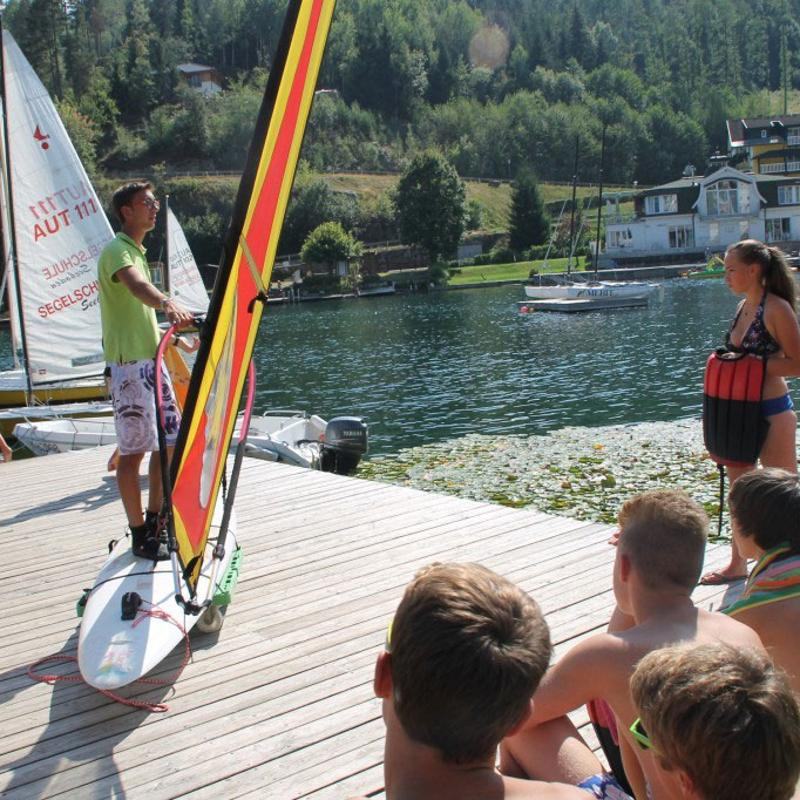 Im Lerncamp Sommerferien erklärt ein Betreuer den Kindern die Technik des Windsurfens