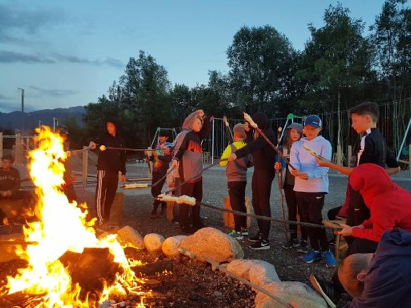 Die Kinder des Ferienlager Innsbruck stehen an einem Lagerfeuer und machen Stockbrot
