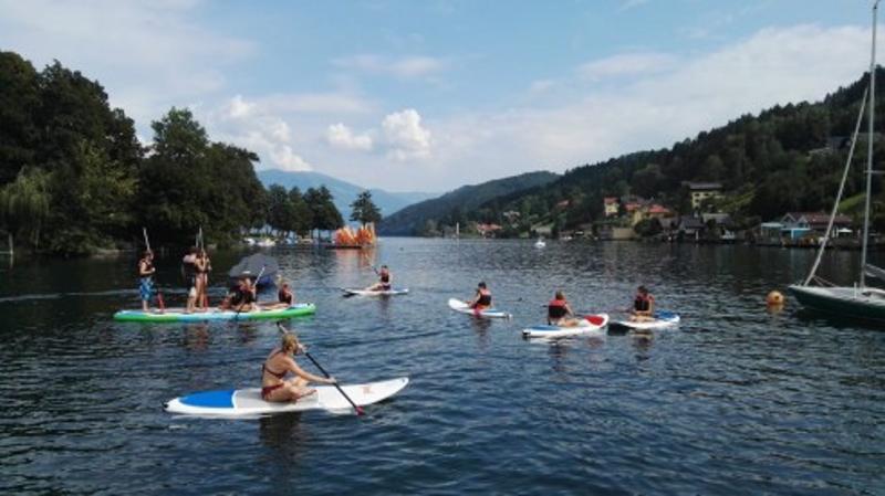 Die Teilnehmer einer Jugendreise Österreich paddeln auf SUP Boards auf dem See