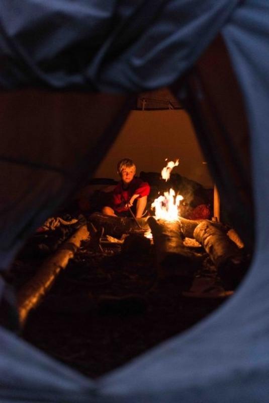Ein Junge sitzt an einem Lagerfeuer und genießt den Abend im Offline-Camp