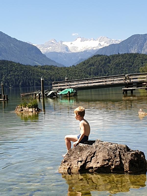 Junge sitzt auf Stein im Wasser im Sommercamp für Kinder
