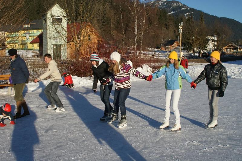 Teilnehmer halten sich gegenseitig beim Eislaufen im Winter-Camp für Kinder