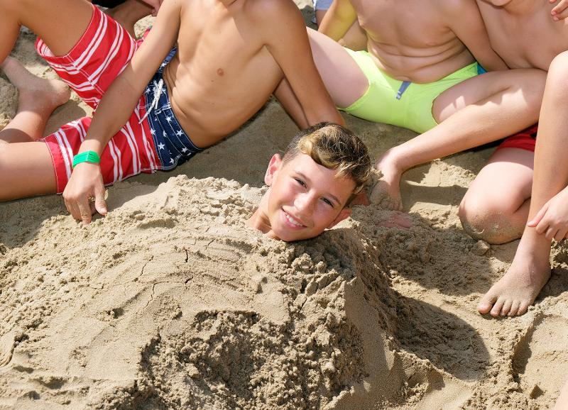 Junge ist eingebuddelt im Sand im Englisch Sommercamp bei Barcelona