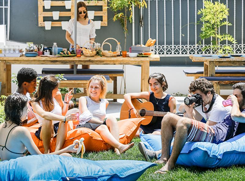 Teilnehmer eines Surf-Camps Portugal sitzen auf Säcken in einem Kreis und spielen Gitarre und singen