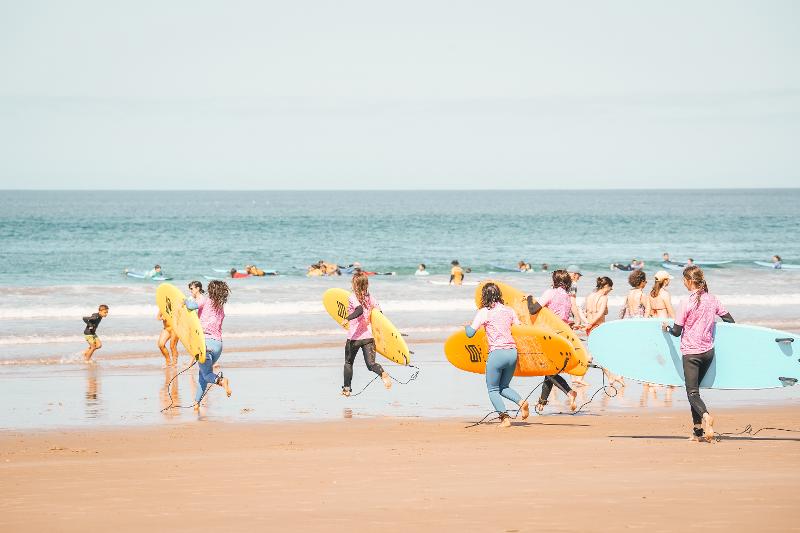  Eine Gruppe Kinder läuft mit Surfbrettern ins Meer bei den Surfcamps Lissabon