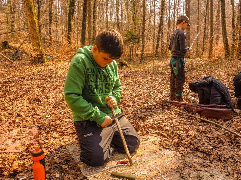 Junge beim Holzschnitzen im Wald in einem Feriencamp in Oberösterreich