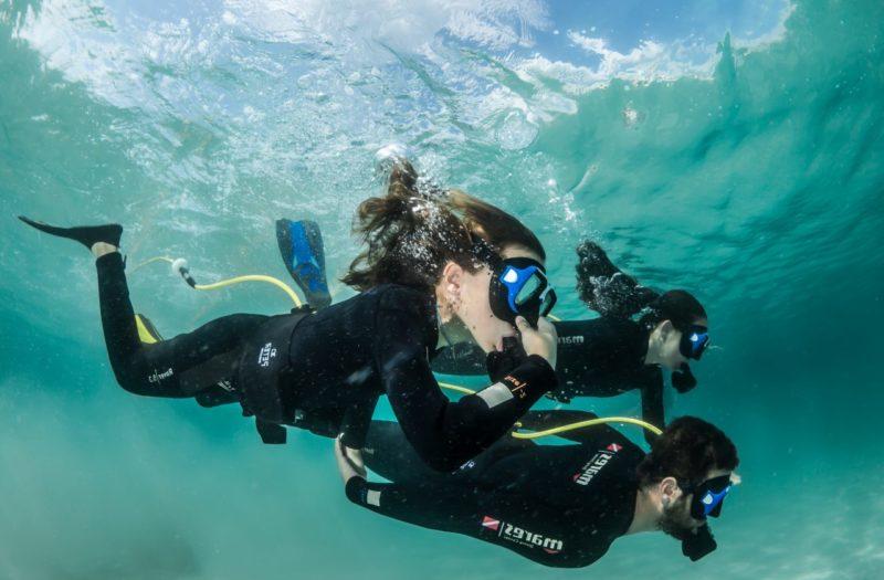 Teilnehmer eines Tauchcamps schwimmen mit einem Tauchlehrer unterwasser
