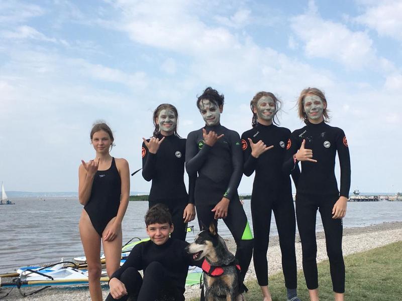 Eine Gruppe Kinder steht in Neoprenanzügen am Strand und lächelt