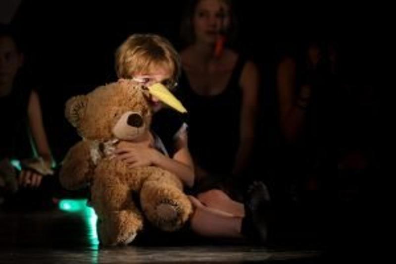 Ein Junge des Englisch-Musicalcamps sitzt mit einem Teddybären auf der Bühne