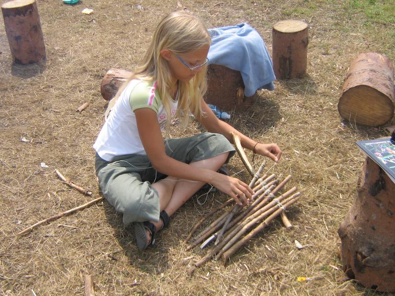 Ein Mädchen bearbeitet Holzstäbe im Survival-Feriencamp