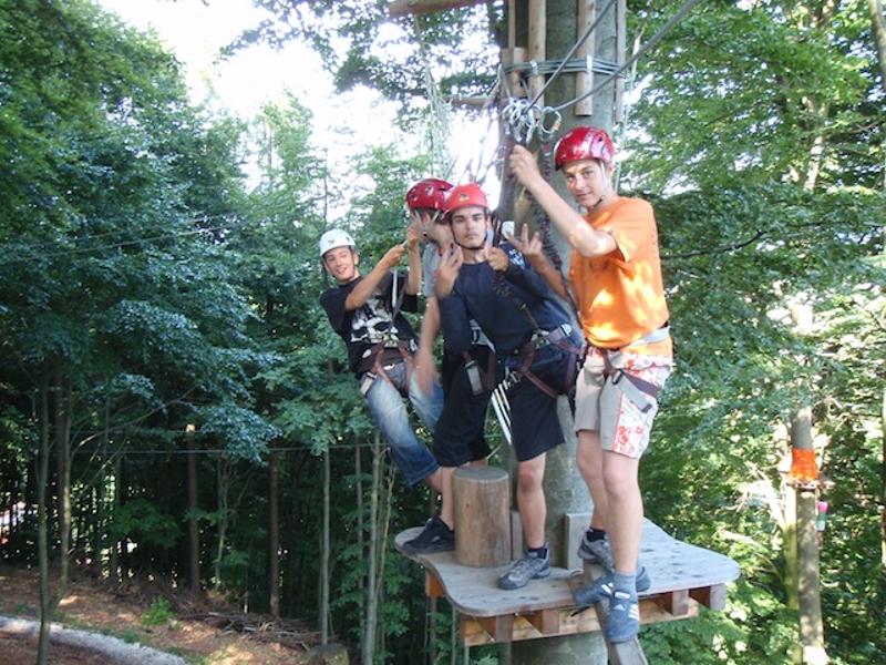 Vier Jungen klettern mit Sicherheitsgurten in einem Hochseilgarten während eines Feriencamps in Österreich