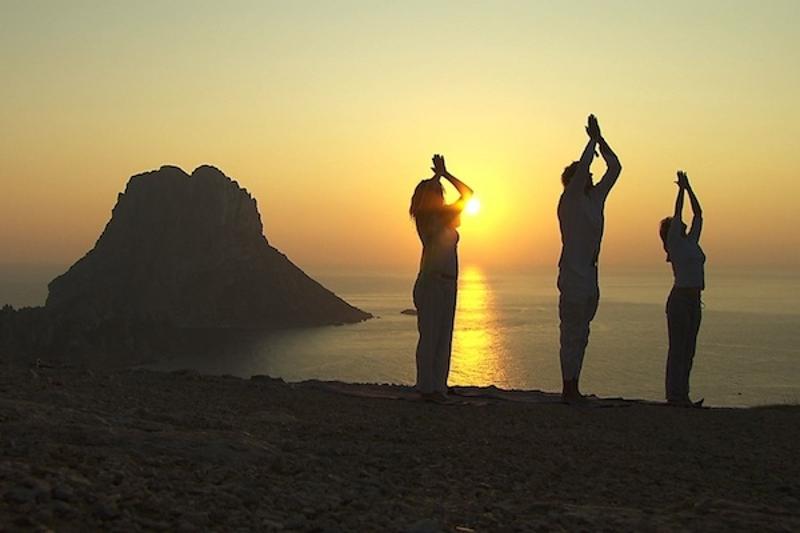 Drei Teilnehmerinnen eines Beach Camps üben Yoga beim Sonnenuntergang